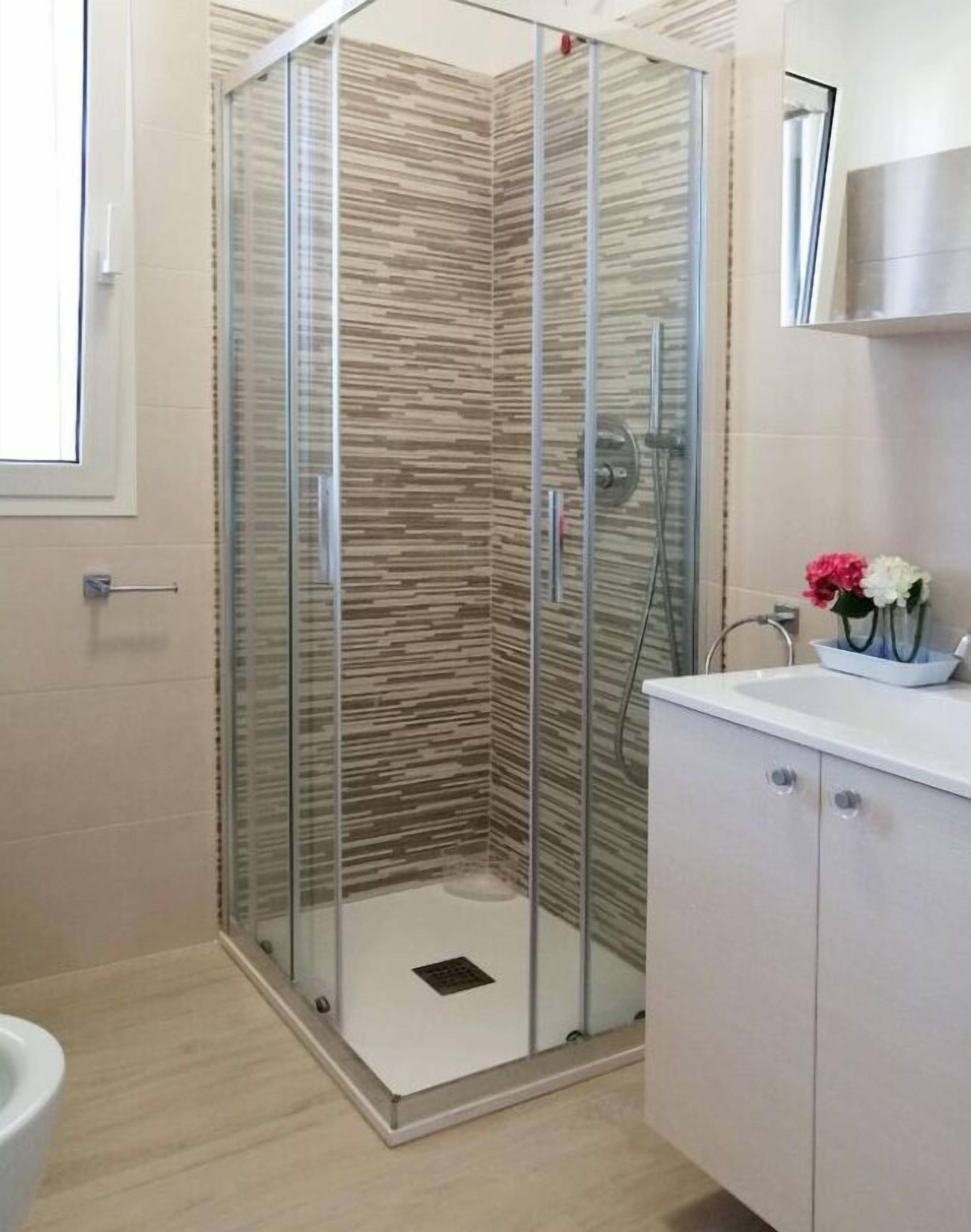 A modern bathroom with a glass shower enclosure, a white sink, and a cabinet with a mirror above it.
