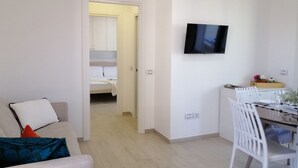 A modern living room with a sofa, a dining table with chairs, and a TV mounted on the wall. - Holihome_La Gioia Tortoreto (Tortoreto Lido)
