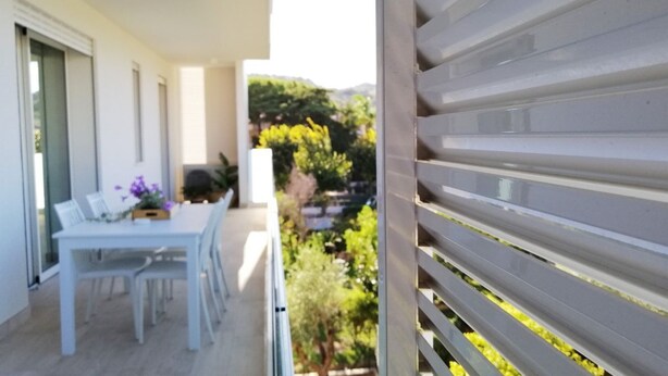 A balcony with a white table and chairs, a potted plant, and a view of greenery and buildings in the background. - Holihome_La Gioia Tortoreto (Tortoreto Lido)