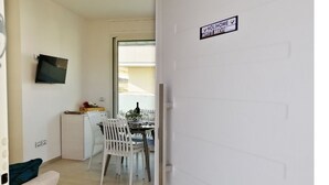 A modern kitchen with white appliances, a dining area with white chairs, and a flat-screen TV mounted on the wall. - Holihome_La Gioia Tortoreto (Tortoreto Lido)