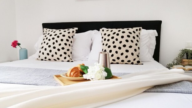 A neatly made bed with polka dot pillows, a tray with croissants and flowers, and a bedside table with a book and a vase. - Holihome_Open House FRN (Alba Adriatica)