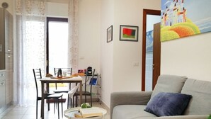 A living room with a sofa, a dining table with chairs, a coffee machine, and a small table with a book. - Holihome_Open House FRN (Alba Adriatica)