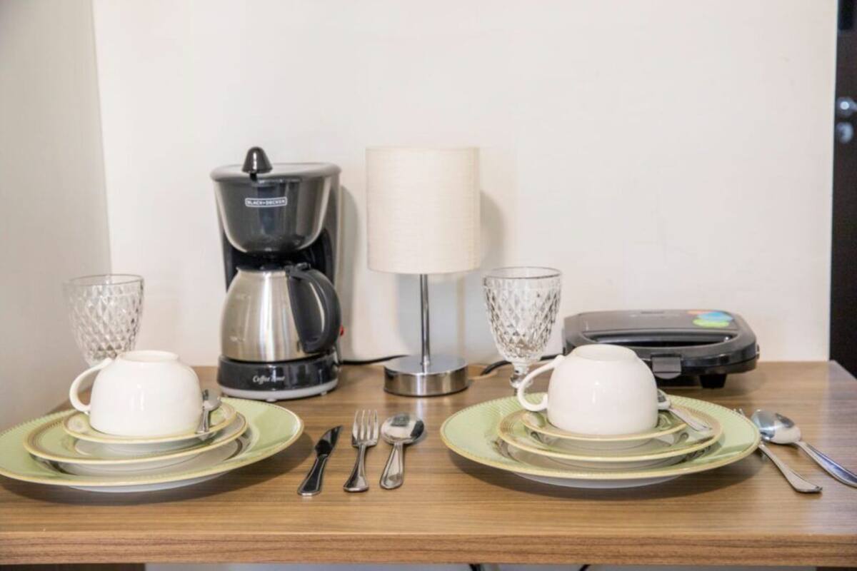 A breakfast setup with two white cups on green plates, a coffee maker, a lamp, and a toaster.