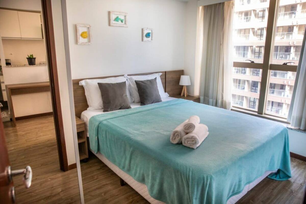 A hotel room with a bed, a nightstand, a window with a view of buildings, and a door leading to a bathroom.
