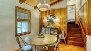 A wooden interior with a round dining table, chairs, a chandelier, a staircase, and a window with blinds. - Fika on The Guadalupe- a charming RIVERFRONT retreat that sleeps 13. (Seguin)