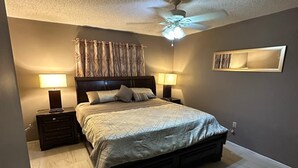 A bedroom with a large bed, two bedside tables with lamps, a ceiling fan, and a wall-mounted mirror. - Charming 3-bedroom house in pleasant Port Richey with AC, WiFi (Port Richey)