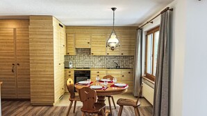 Une cuisine en bois avec une table à manger pour quatre personnes, un four encastré et une fenêtre avec des rideaux.