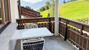 Un balcon avec une table et des chaises, donnant sur une colline verdoyante et des montagnes.
