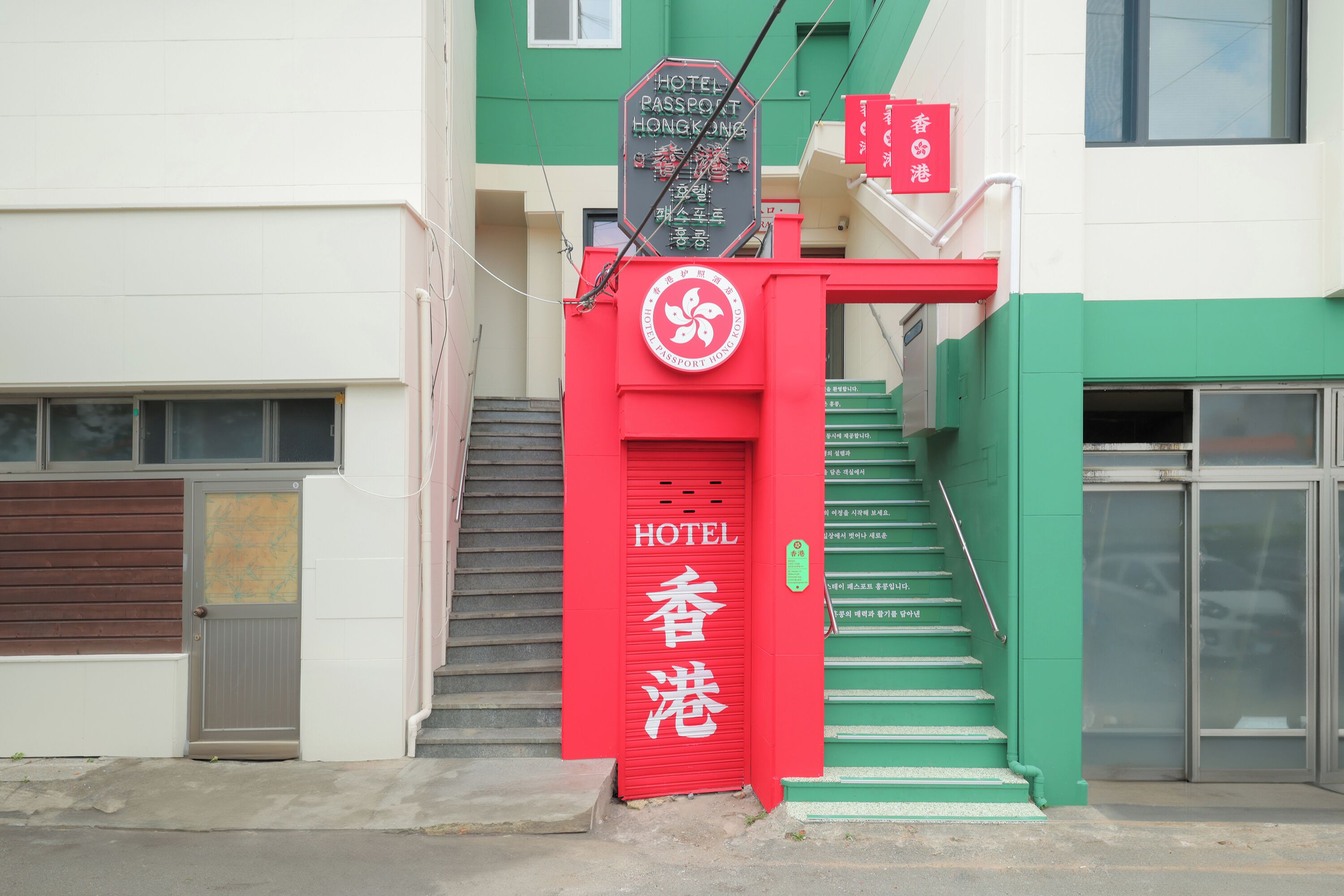Entrada de hotel con un letrero rojo que indica el nombre y una escalera que conduce a la entrada.