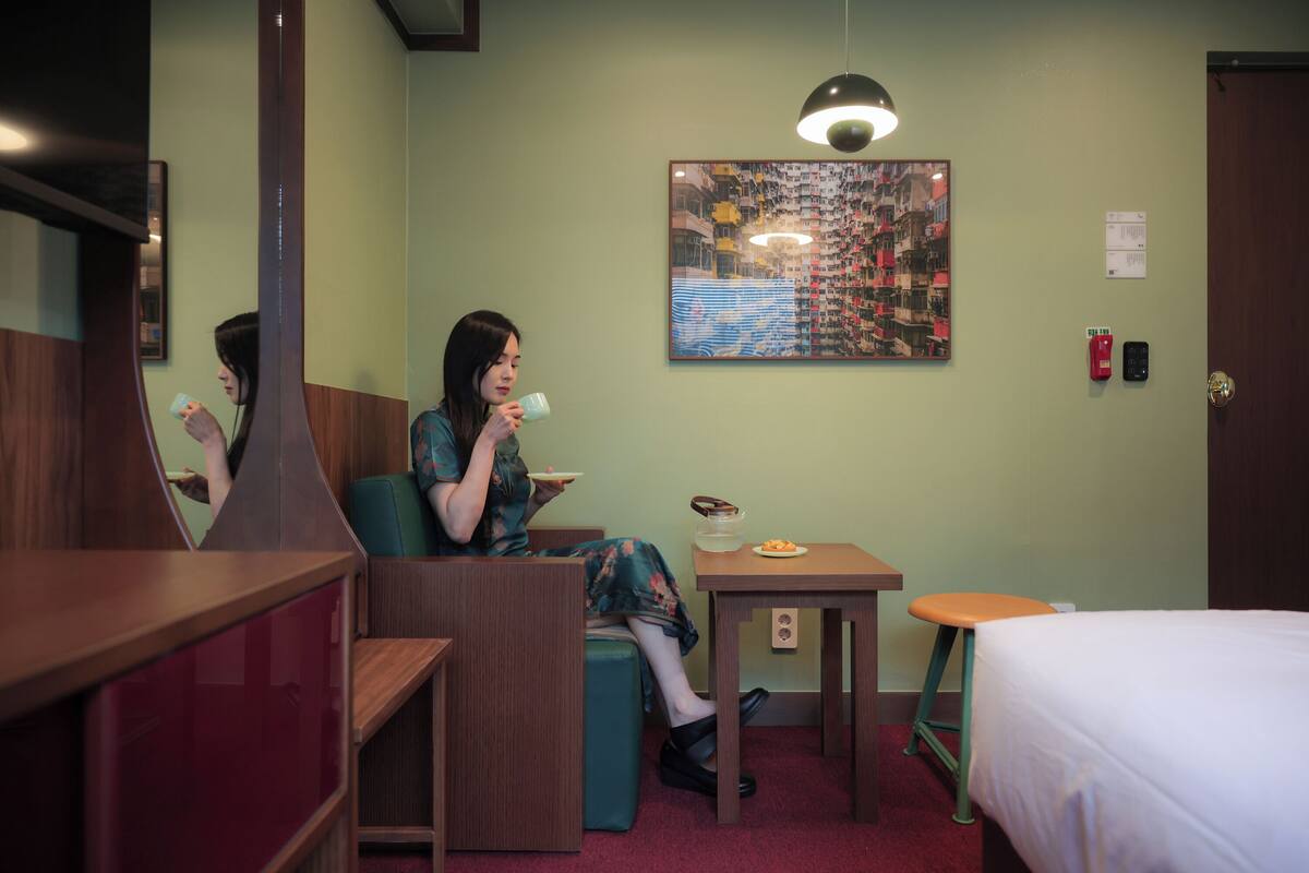 A room with a bed, a table with a bowl of fruit, a chair, and a mirror.