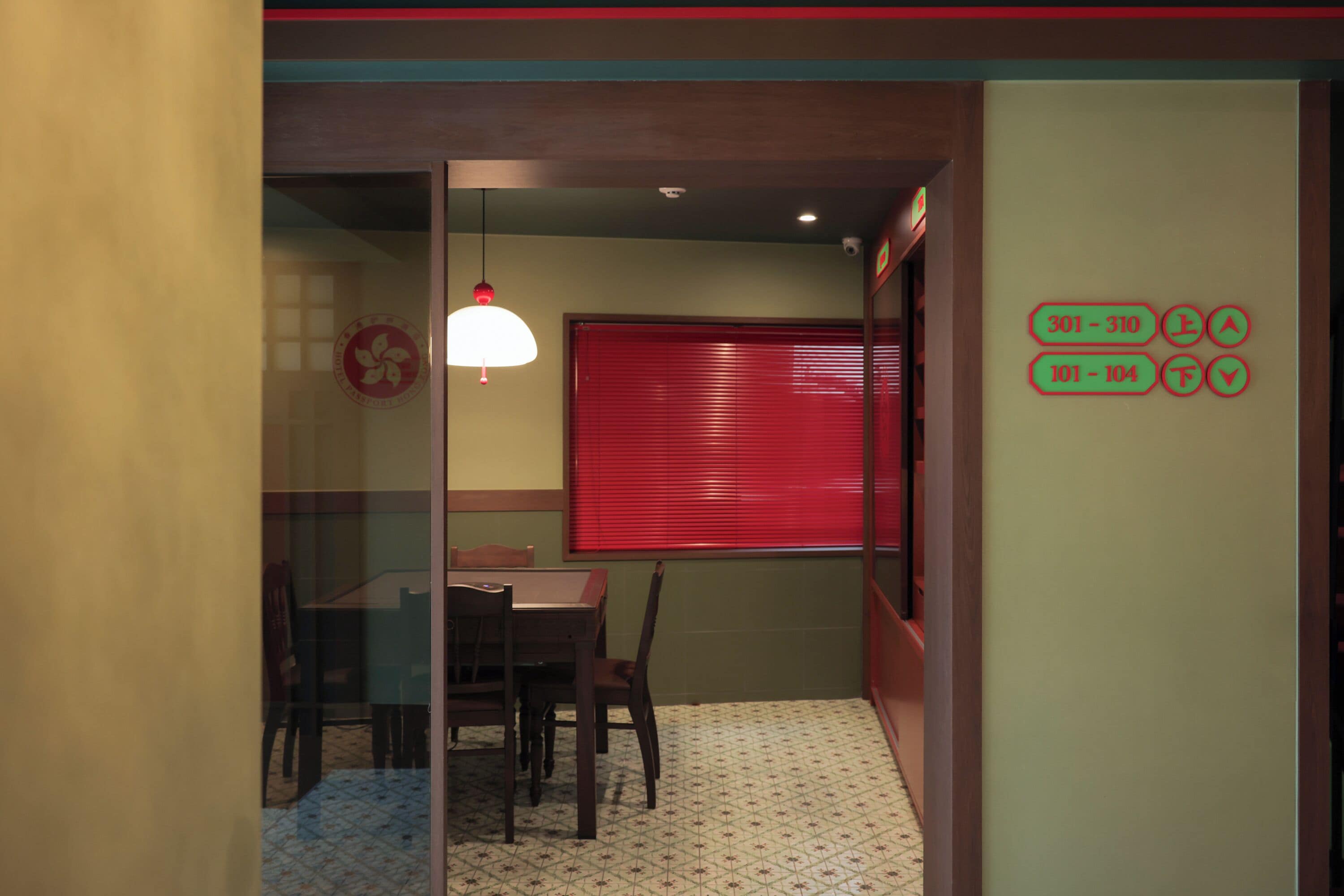 A room with a dining table and chairs, a red window, and a wall with emergency contact numbers.
