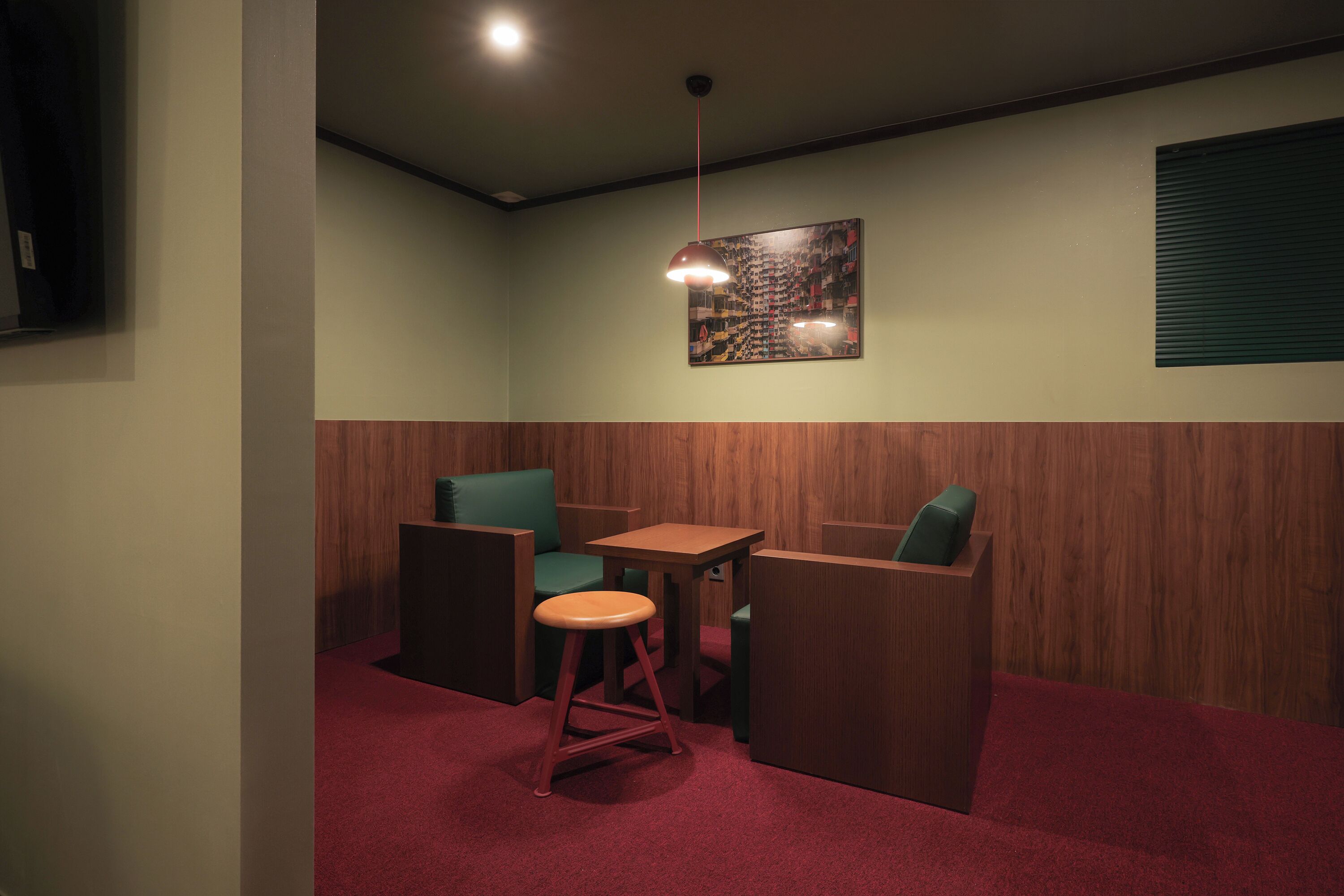 Ein Zimmer mit einer Holzwand, einem Tisch, zwei Stühlen und einem Hocker, sowie einer Pendelleuchte.