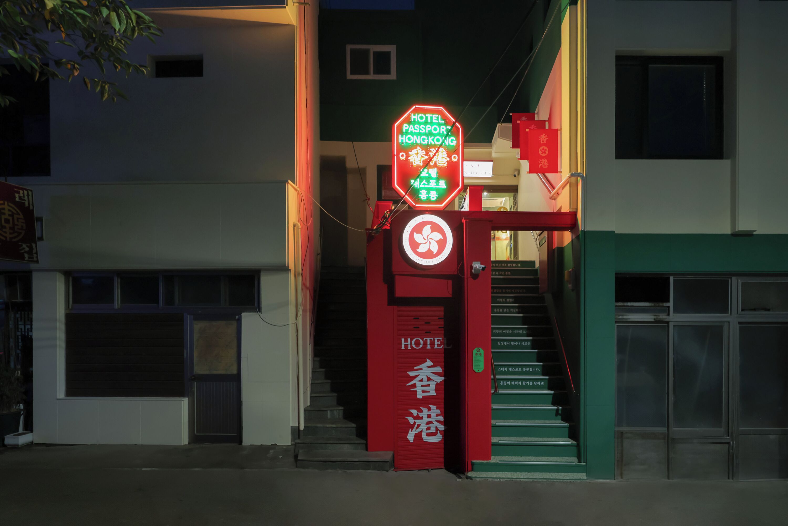 A hotel entrance with a neon sign indicating 'HOTEL PASSPORT HONGKONG' and a red sign with 'HOTEL' and Chinese characters.
