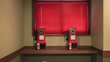 Two red rotary phones on a wooden counter with a red window above them.