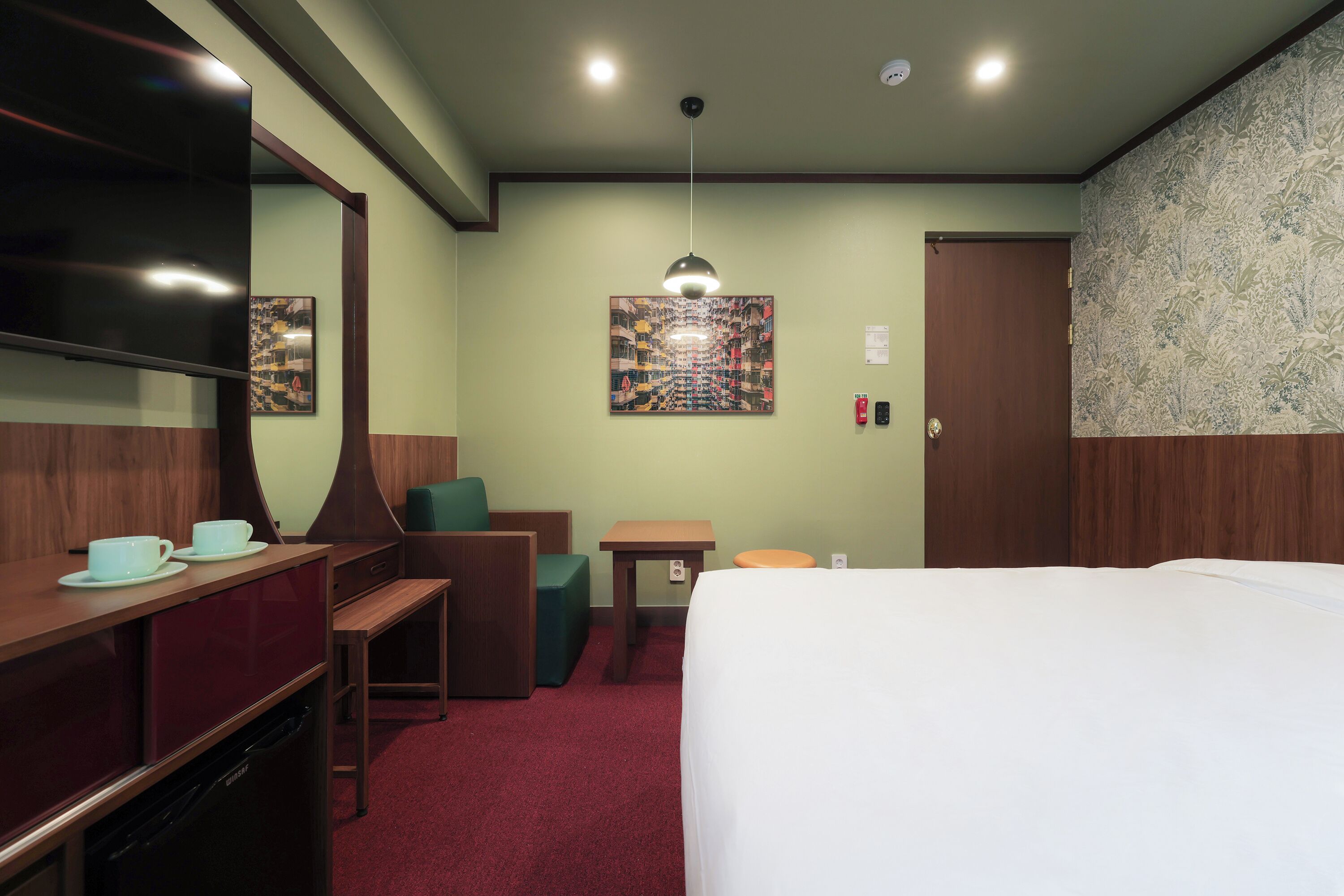 Ein Hotelzimmer mit einem Bett, einem Schreibtisch mit Stuhl, einem kleinen Tisch, einer Couch und einem an der Wand befestigten Fernseher.