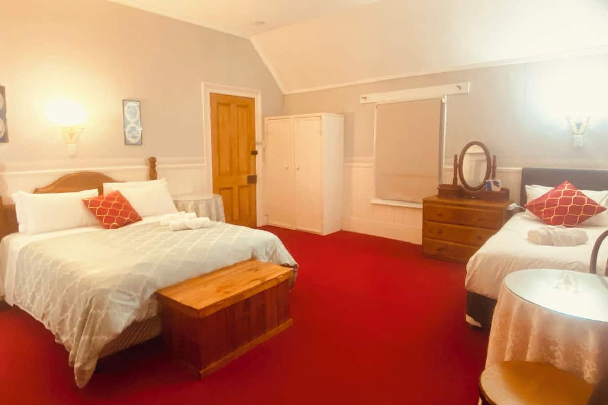 Quarto de hotel com duas camas, um banco de madeira, cômoda, espelho e tapete vermelho.