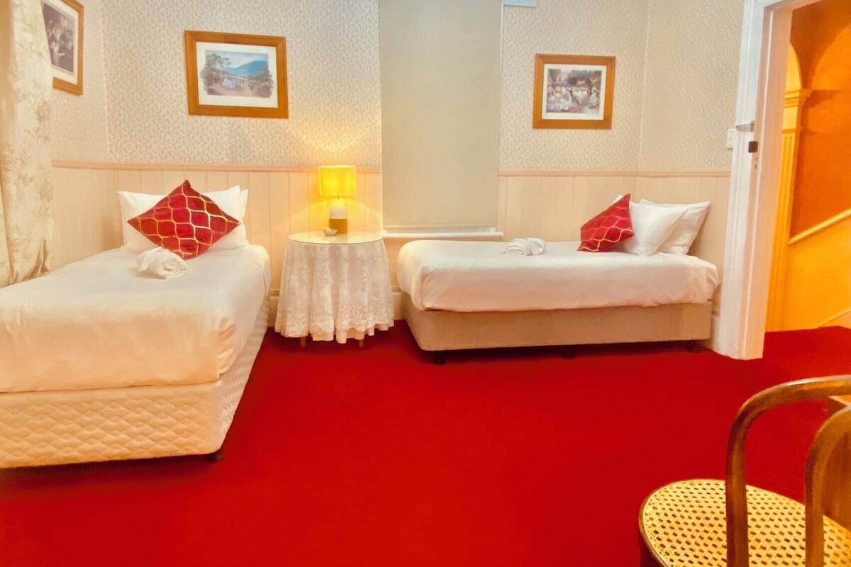 Quarto de hotel com duas camas de solteiro, uma mesinha redonda com abajur e um espelho grande na parede.