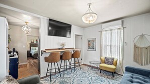 Una sala de estar moderna con un tapete azul estampado, un sofá gris, un sillón amarillo y una zona de bar con taburetes.
