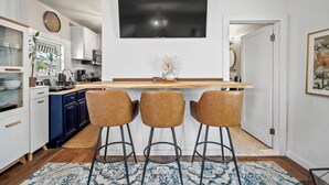 Una cocina moderna con armarios blancos, encimera de madera y tres taburetes marrones.
