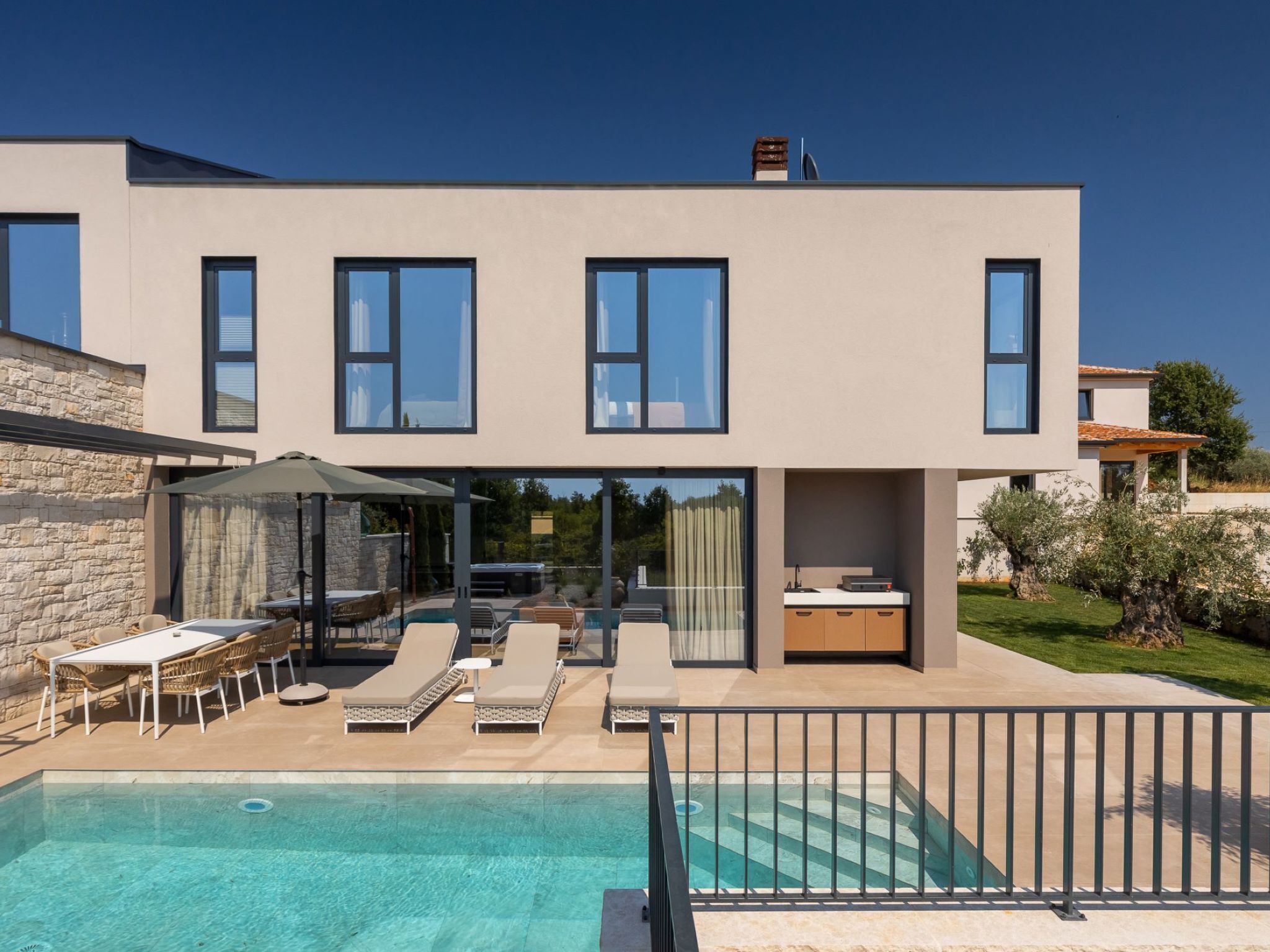 Une maison moderne à deux étages dotée d’une piscine, d’un espace extérieur aménagé et d’un coin cuisine.