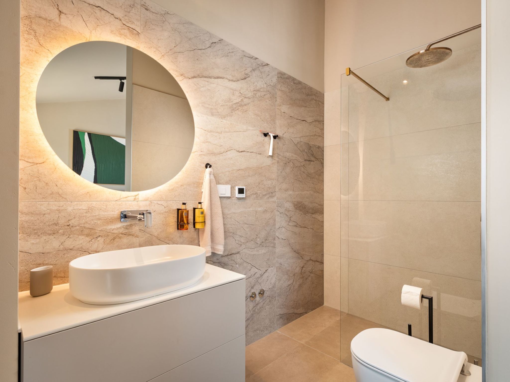 A modern bathroom with a round mirror, a white sink, and a shower area.