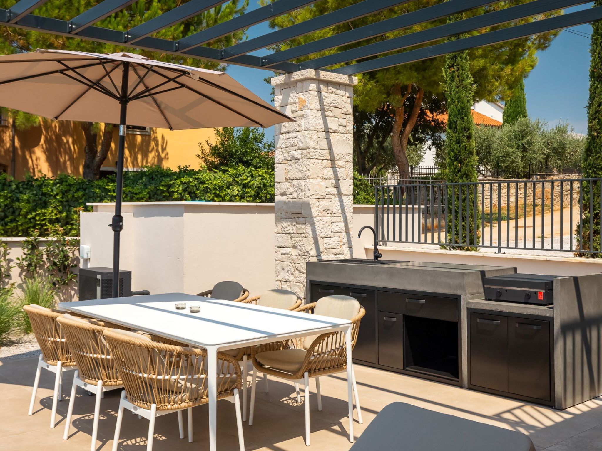 An outdoor patio with a stone pillar, a grill, a table with chairs, and an umbrella.