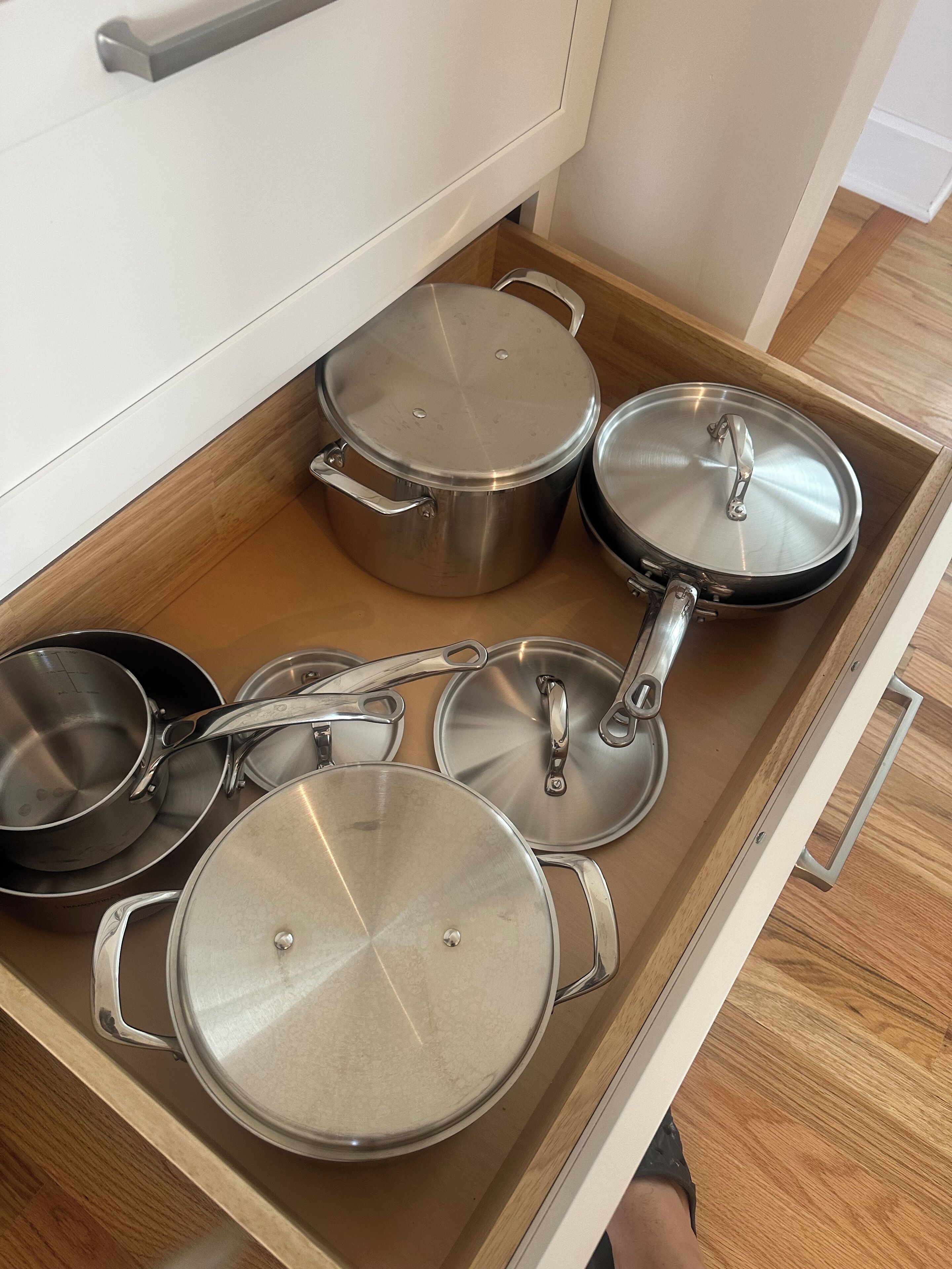 A kitchen drawer with various stainless steel pots and pans.