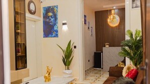 Un vestíbulo de hotel moderno con un mostrador de recepción de mármol, un sofá con un cojín rojo, una planta grande en maceta y una obra de arte enmarcada en la pared.