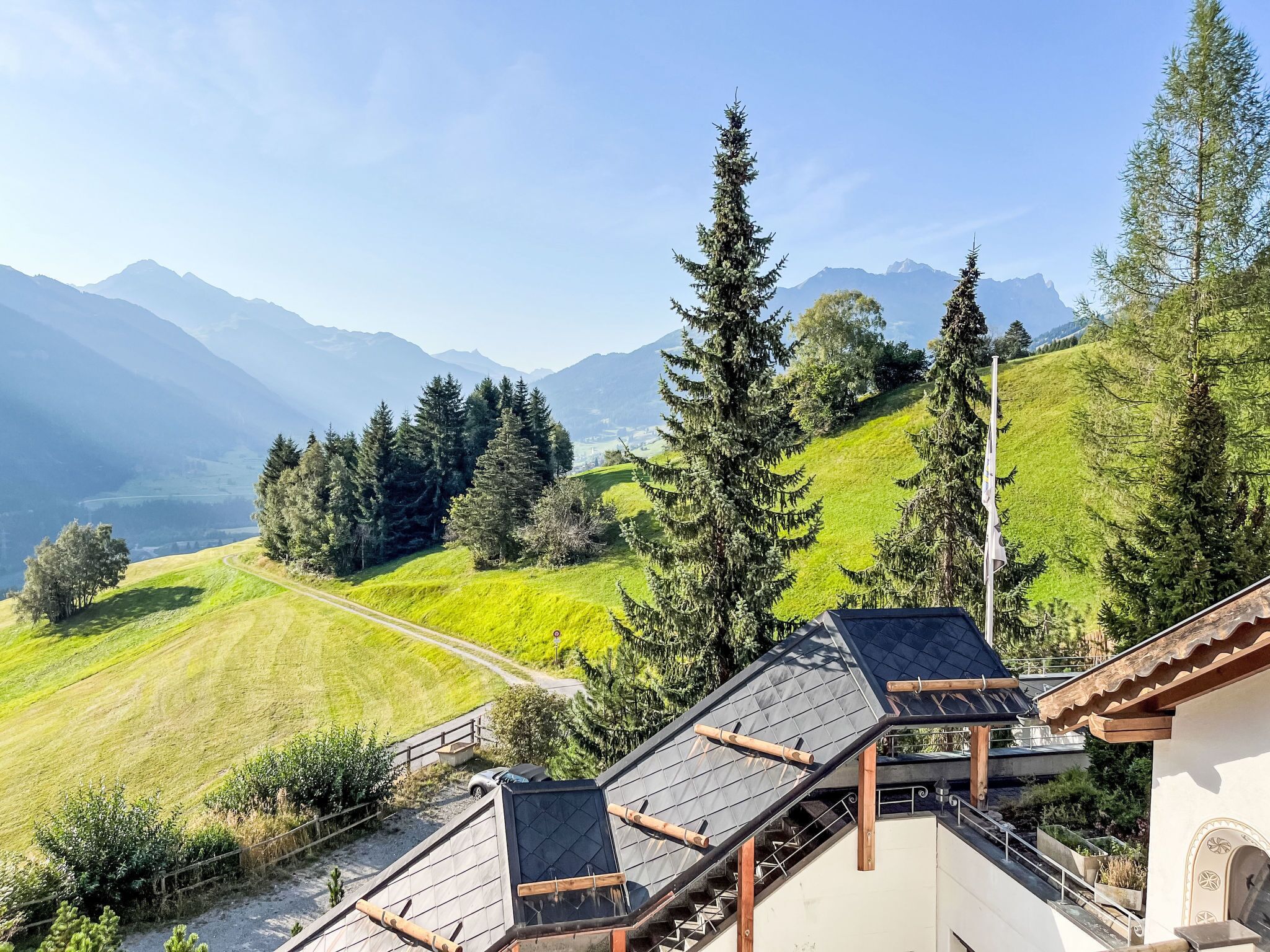 Une vue sur une montagne, avec un sentier menant à un bâtiment doté d’un toit en pente et de poutres en bois.