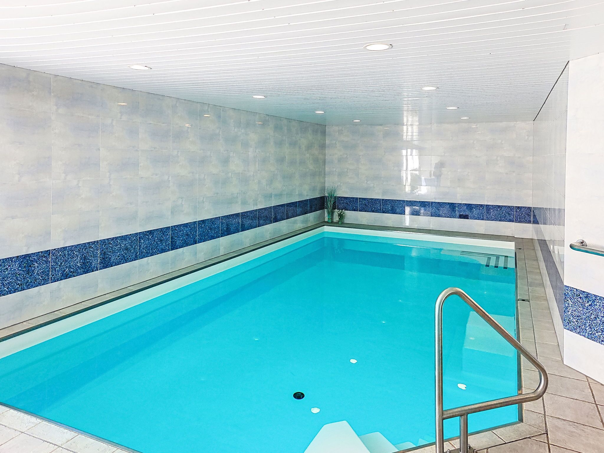 Une piscine intérieure à l’eau d’un bleu limpide, avec des murs carrelés et un escalier en métal.
