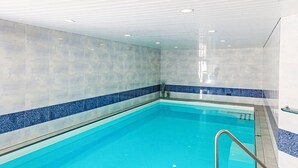 An indoor swimming pool with clear blue water, tiled walls, and a metal ladder. - Toissa A4 by Interhome (Savognin)