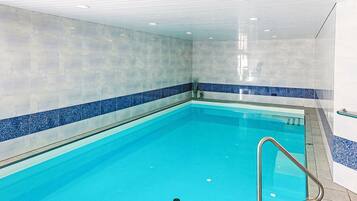 Une piscine intérieure à l’eau d’un bleu limpide, avec des murs carrelés et un escalier en métal.