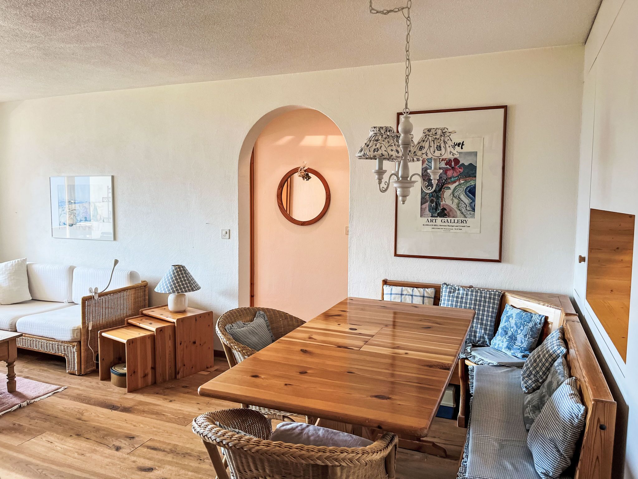 Un salon chaleureux avec une table à manger en bois, des meubles en osier, un canapé blanc et, au mur, un tableau encadré provenant d’une galerie d’art.