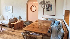 A cozy living room with a wooden dining table, wicker furniture, a white sofa, and a framed art gallery picture on the wall. - Toissa A4 by Interhome (Savognin)