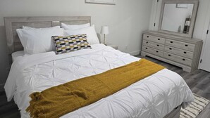 A bedroom with a bed, a nightstand, a dresser, and a mirror.