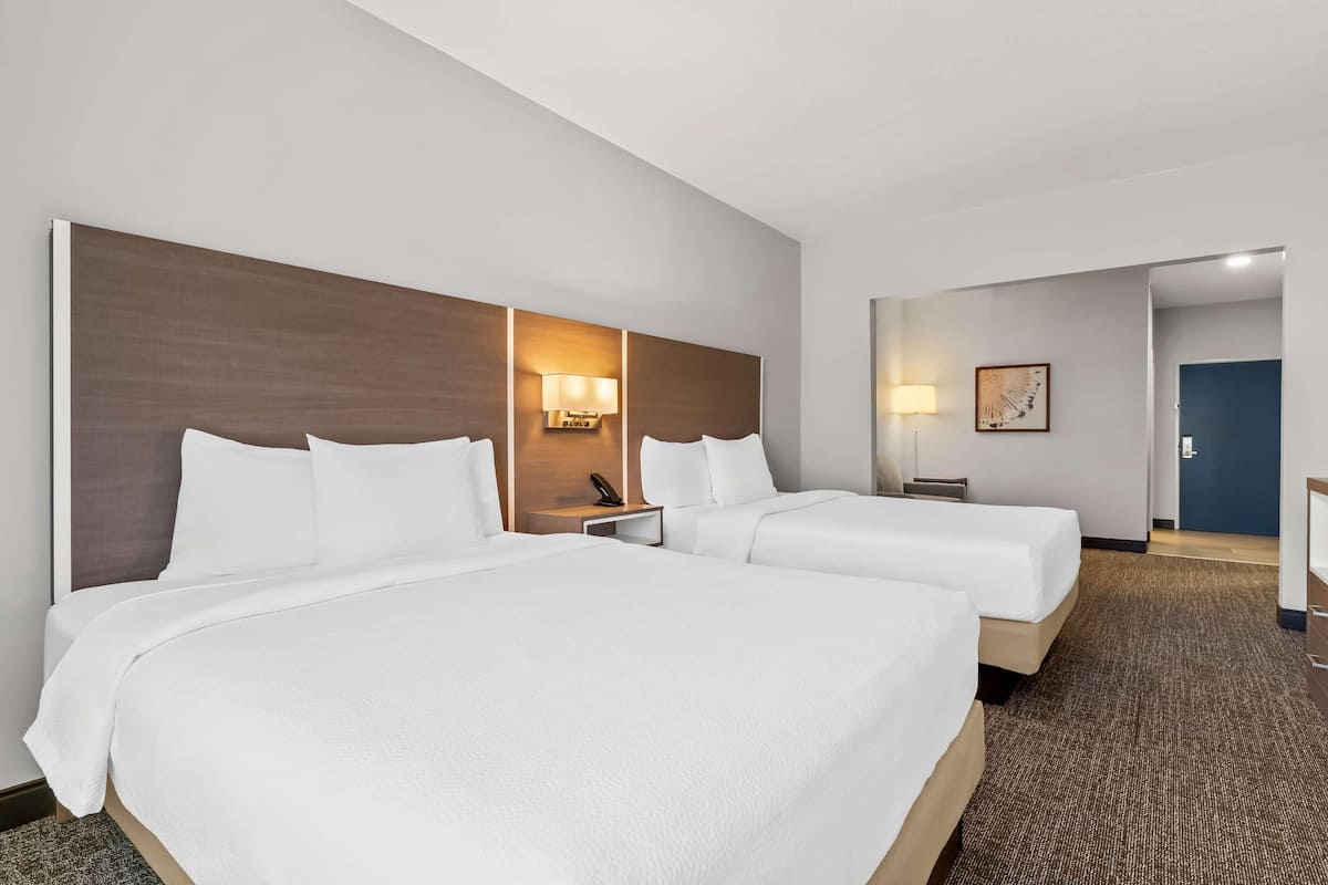 Habitación de hotel con dos camas, cabecero, lámparas de noche, escritorio y una puerta.