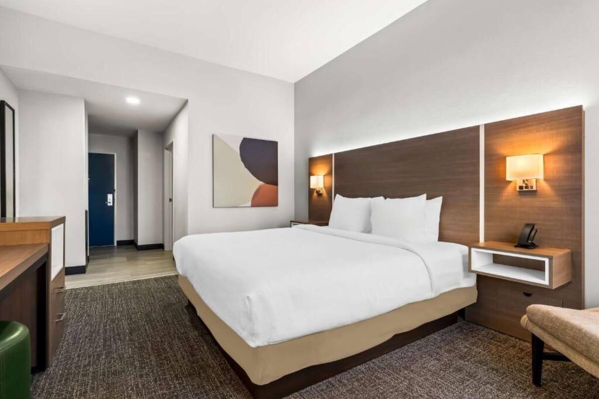 Una habitación de hotel con una cama grande, mesitas de noche, un escritorio y una silla.