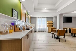 A modern kitchen with a bar area, wooden cabinets, and a dining area with chairs and tables. - Spark by Hilton Catoosa Tulsa (Catoosa)