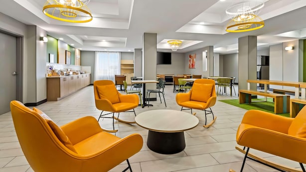 Una hall moderna di un hotel con sedie arancioni vivaci, un tavolo rotondo al centro e lampade a soffitto originali.