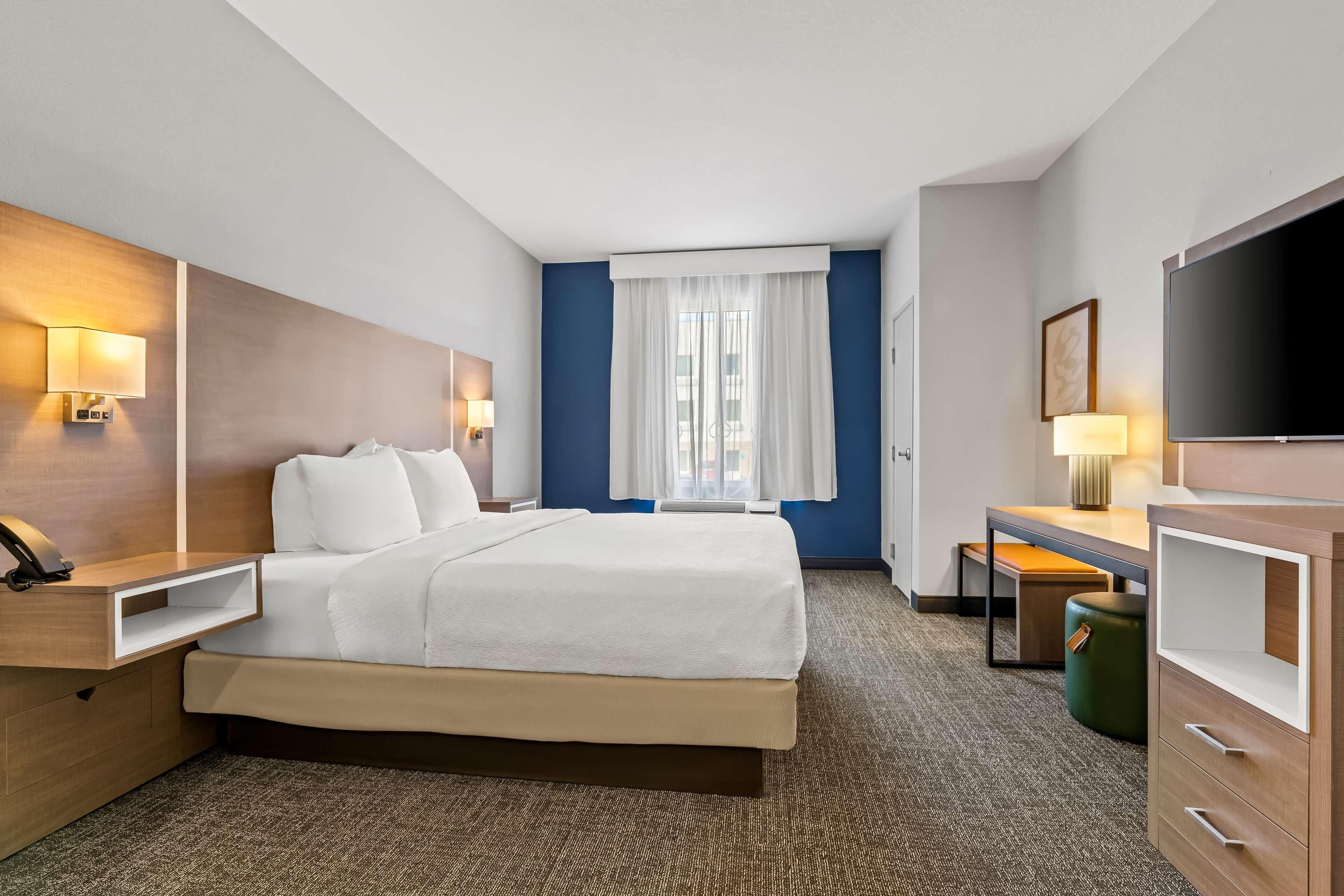 A hotel room with a bed, bedside tables, a desk, a television, and a window with curtains.