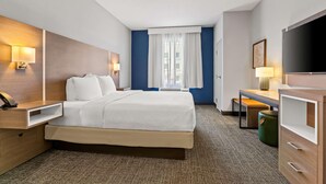 Habitación de hotel con cama, mesitas de noche, escritorio, televisor y ventana con cortinas.