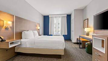 A hotel room with a bed, bedside tables, a desk, a television, and a window with curtains.