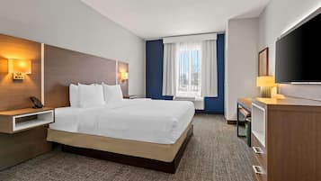 Ein Hotelzimmer mit einem großen Bett, Nachttischen, einem Schreibtisch, einem Fernseher und einem Fenster mit Vorhängen.
