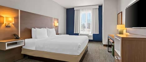 Une chambre d’hôtel avec un grand lit, des tables de chevet, un bureau, une télévision et une fenêtre avec des rideaux.