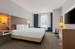 A hotel room with a large bed, bedside tables, a desk, a TV, and a window with curtains.