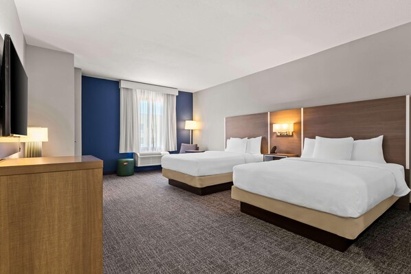 Una habitación de hotel con dos camas, un escritorio, un televisor y una ventana con cortinas.