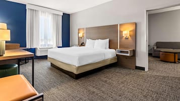 A hotel room with a bed, a desk, a chair, a sofa, and a lamp.