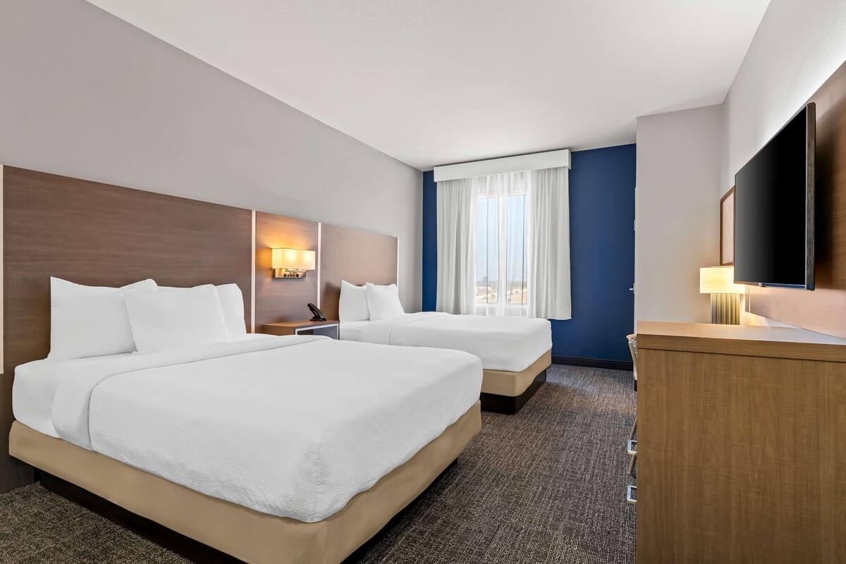 Habitación de hotel con dos camas, un escritorio, un televisor y una ventana con cortinas.
