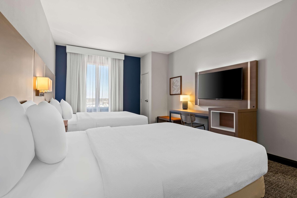 Habitación de hotel con dos camas, un escritorio, televisor y ventana con cortinas.
