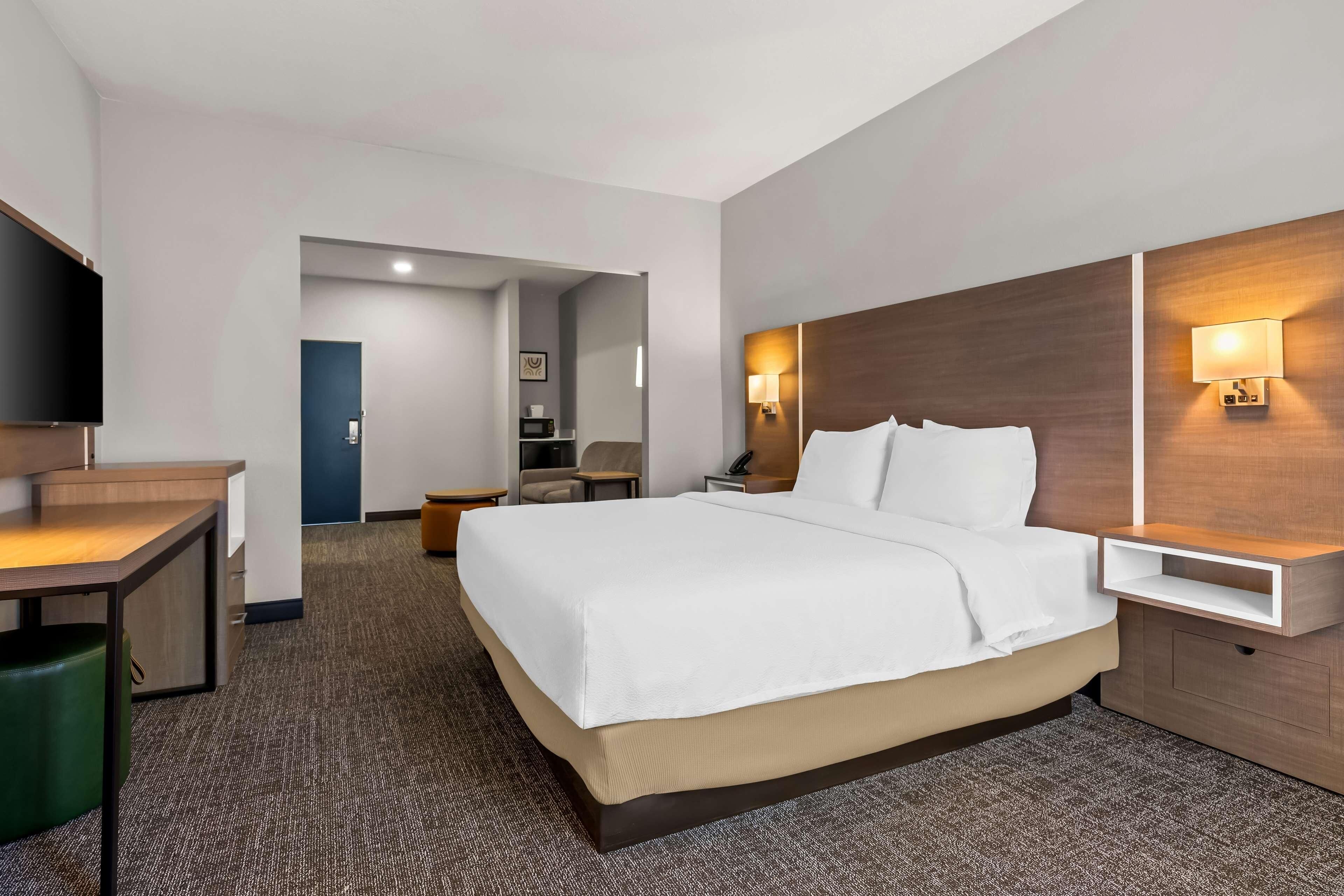 Ein Hotelzimmer mit einem Bett, einem Schreibtisch, einem Stuhl, einem Fernseher und einem Nachttisch mit Lampe.